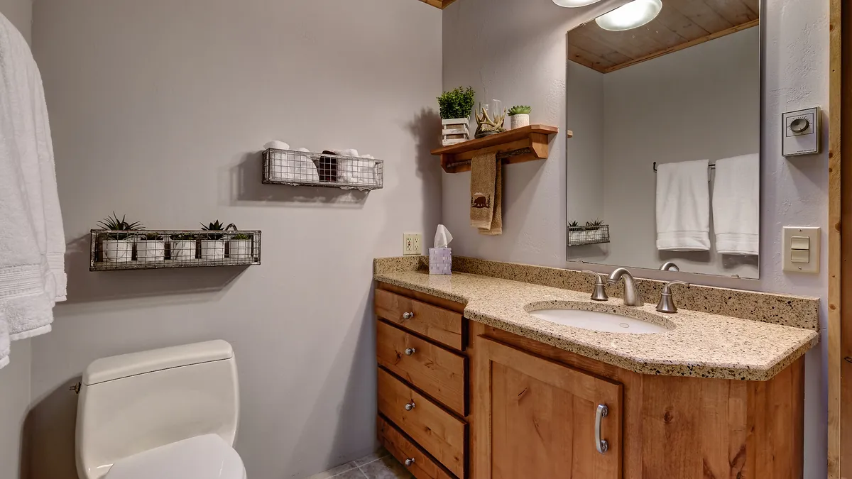 A serene bathroom scene with a vanity and sink, a toilet, decorative shelving, and a large mirror. The mood is calm and refreshing, suggesting an inviting space for self-care and relaxation after a day spent exploring or enjoying the outdoors.