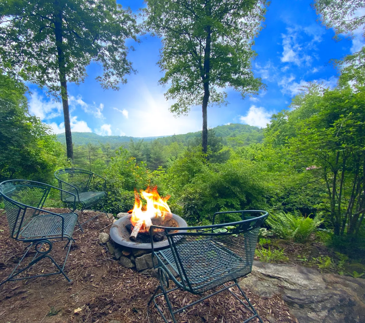 Set outdoors, this scene features a stone fire pit surrounded by comfortable seating, all nestled in natural surroundings. The fire pit glows warmly, inviting guests to gather, share stories, and enjoy the crisp mountain air in comfort.