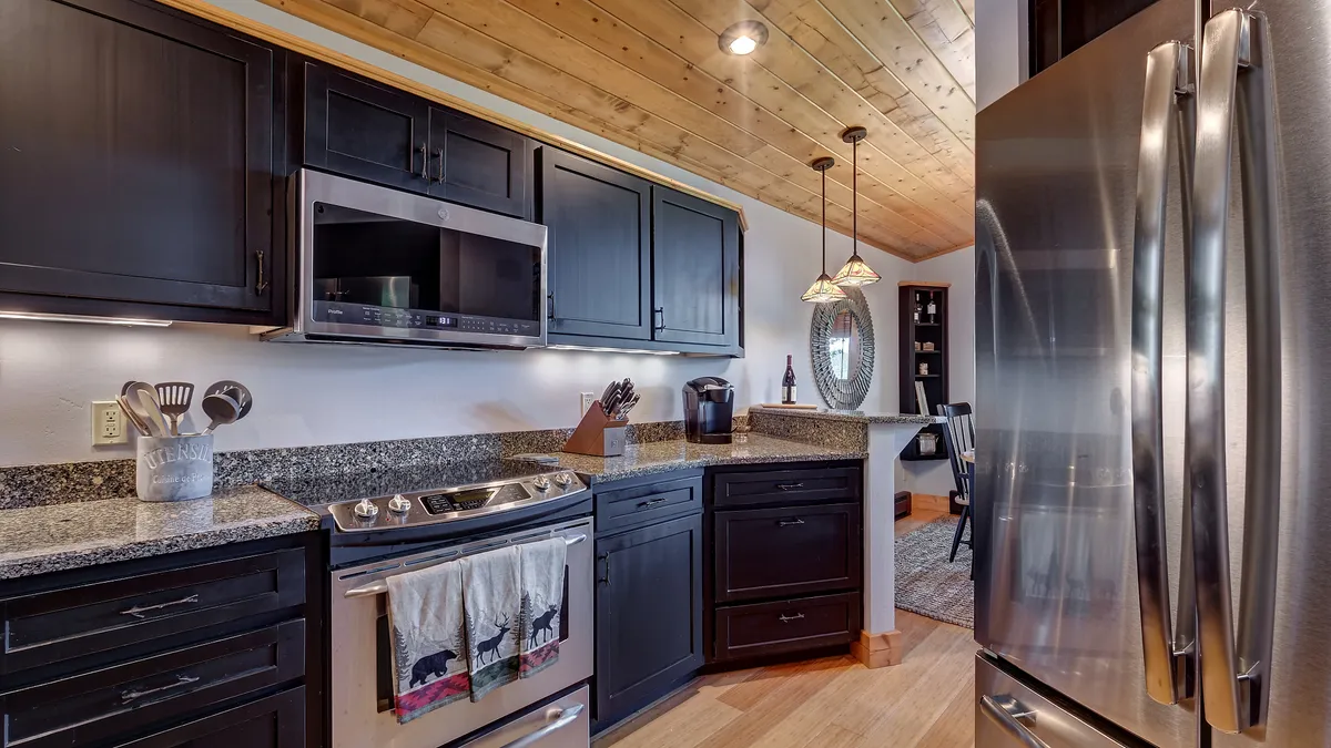 A cozy and modern kitchen with gleaming stainless steel appliances, a polished granite countertop, and a warm wooden ceiling. The decorative mirror adds depth, while the open layout suggests a space perfect for gathering and preparing meals together.