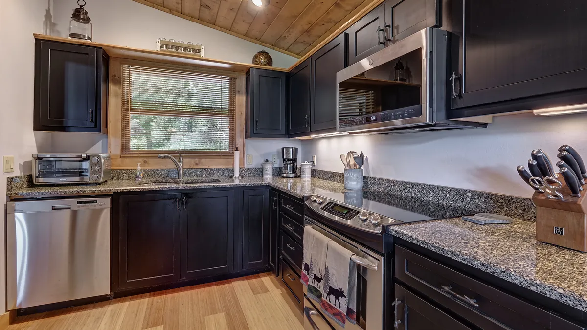 A bright, welcoming kitchen with black cabinetry, granite countertops, and modern stainless steel appliances. Sunlight streams through a window, illuminating spacious counters ideal for meal prep and family cooking. The kitchen feels both functional and inviting, perfect for gathering and culinary activity.