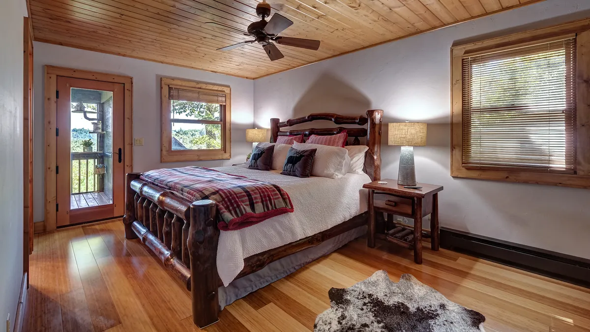 A spacious master bedroom featuring a king-sized bed with plaid bedding, warm wooden furniture, and large windows that let in abundant natural light. Decorative lamps and serene decor add to the relaxing atmosphere, making it an inviting retreat after a long day.