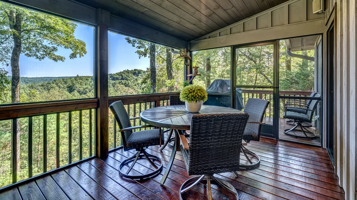 An outdoor dining setup on a porch, featuring a table with chairs surrounded by greenery and a decorative plant. The tranquil setting invites guests to enjoy meals al fresco, whether it’s morning coffee or an evening barbecue.